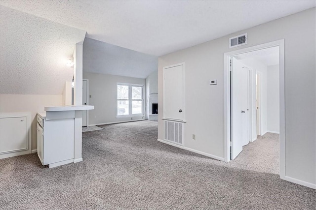 unfurnished living room featuring carpet, lofted ceiling, visible vents, a fireplace with raised hearth, and a textured ceiling