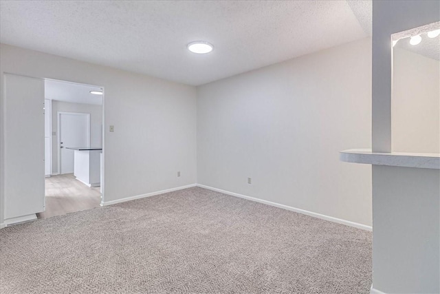 empty room featuring baseboards, a textured ceiling, and light colored carpet