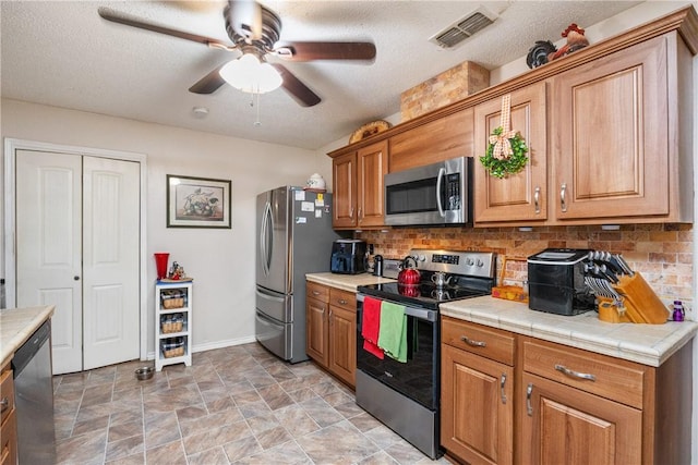 kitchen with tile countertops, a textured ceiling, backsplash, and stainless steel appliances