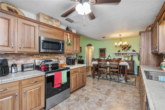 kitchen with tile countertops, backsplash, hanging light fixtures, a textured ceiling, and appliances with stainless steel finishes