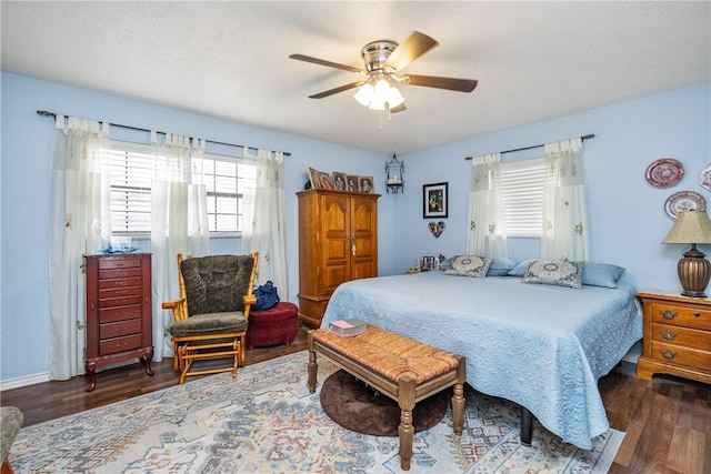 bedroom with a textured ceiling, ceiling fan, dark wood-type flooring, and multiple windows