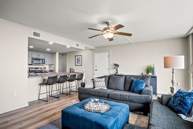 living room featuring ceiling fan, sink, and light wood-type flooring