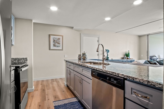 kitchen with gray cabinetry, stainless steel appliances, dark stone counters, sink, and light hardwood / wood-style flooring