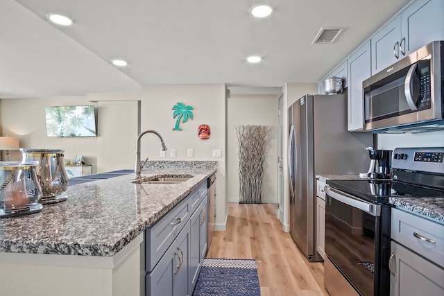 kitchen with appliances with stainless steel finishes, stone countertops, light hardwood / wood-style flooring, sink, and a kitchen island with sink