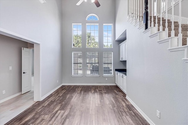 unfurnished living room featuring dark hardwood / wood-style flooring, a towering ceiling, and ceiling fan