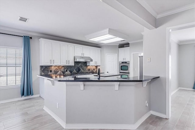 kitchen featuring white cabinets, a kitchen breakfast bar, kitchen peninsula, and crown molding