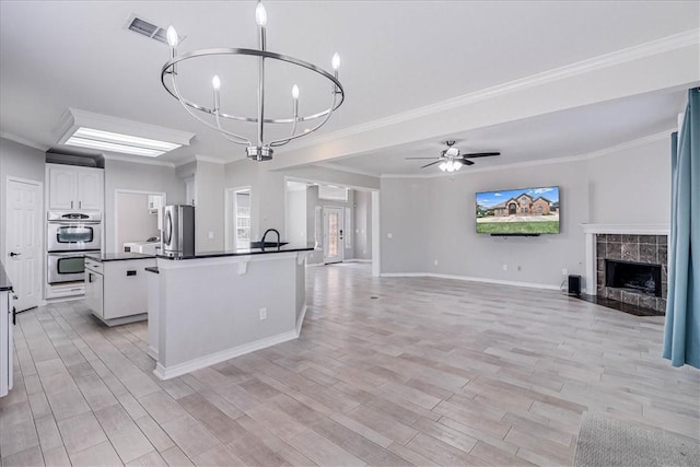 kitchen with light wood-type flooring, ornamental molding, stainless steel appliances, a kitchen island with sink, and white cabinetry