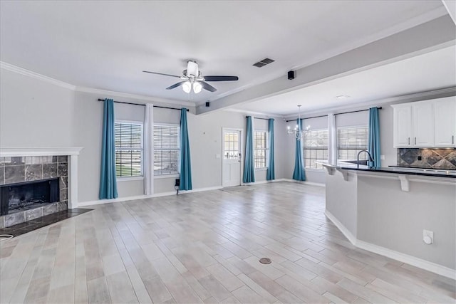 unfurnished living room featuring ceiling fan with notable chandelier, light hardwood / wood-style floors, ornamental molding, and a tile fireplace