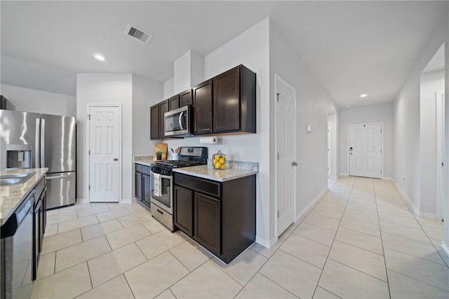 kitchen with dark brown cabinetry, visible vents, appliances with stainless steel finishes, and light stone counters