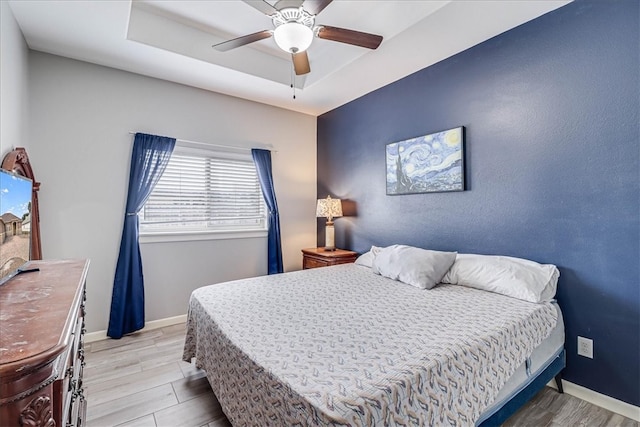 bedroom with ceiling fan, light hardwood / wood-style floors, and a tray ceiling