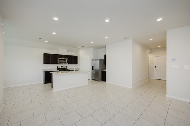 kitchen featuring light stone counters, light tile patterned floors, a center island with sink, and stainless steel appliances