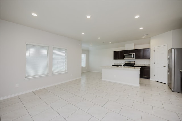 kitchen featuring light tile patterned flooring, sink, light stone counters, appliances with stainless steel finishes, and an island with sink