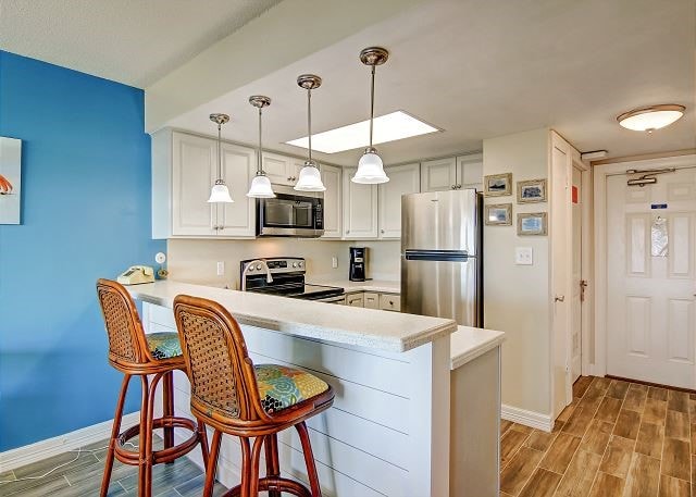 kitchen with kitchen peninsula, appliances with stainless steel finishes, a kitchen bar, and light hardwood / wood-style flooring