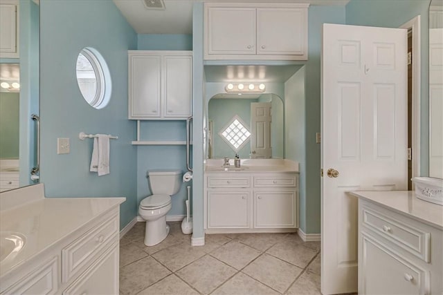 bathroom featuring toilet, tile patterned flooring, baseboards, and two vanities