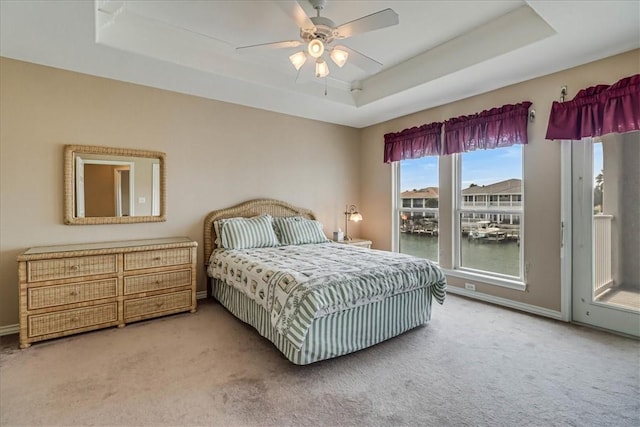 carpeted bedroom featuring a water view, a ceiling fan, access to exterior, baseboards, and a raised ceiling