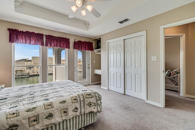 carpeted bedroom with visible vents, baseboards, access to exterior, a tray ceiling, and a closet