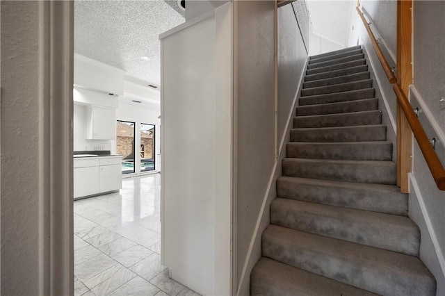 staircase with marble finish floor and a textured ceiling