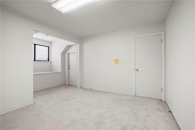 additional living space featuring light carpet, a textured ceiling, and baseboards