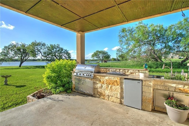 view of patio featuring a water view, an outdoor kitchen, a grill, and sink