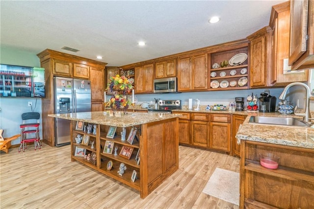 kitchen with sink, light stone counters, light wood-type flooring, a kitchen island, and stainless steel appliances