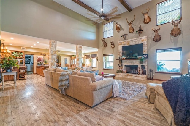 living room featuring a stone fireplace, beamed ceiling, decorative columns, ceiling fan, and light hardwood / wood-style floors