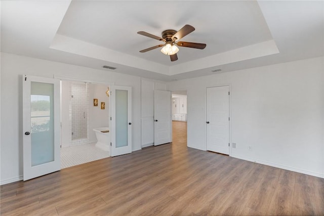 unfurnished bedroom featuring light wood-type flooring, ceiling fan, connected bathroom, and a tray ceiling