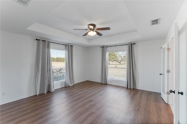 empty room featuring ceiling fan, dark wood-type flooring, and a tray ceiling