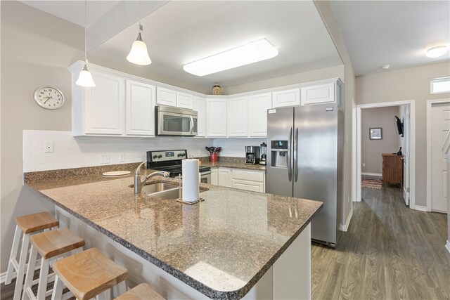 kitchen featuring stainless steel appliances, decorative light fixtures, dark hardwood / wood-style floors, white cabinets, and kitchen peninsula