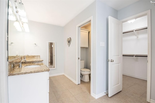 bathroom featuring toilet, baseboards, tile patterned flooring, vanity, and a walk in closet