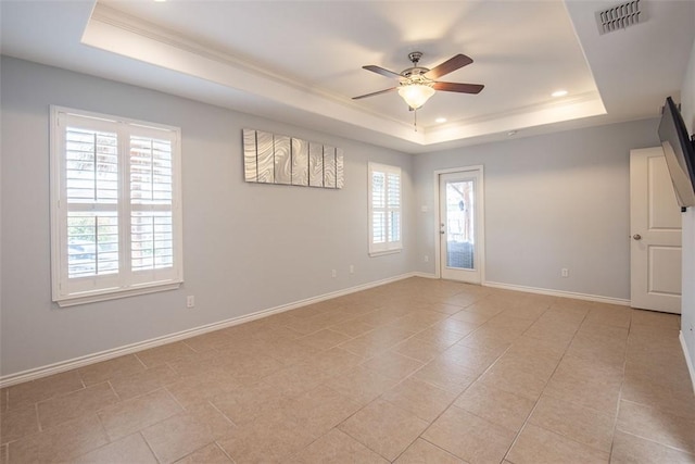 empty room featuring a ceiling fan, baseboards, ornamental molding, visible vents, and a raised ceiling