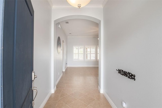 hall featuring crown molding, baseboards, arched walkways, and light tile patterned floors