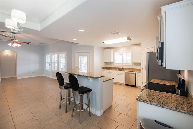 kitchen with a breakfast bar area, a ceiling fan, stainless steel appliances, white cabinets, and crown molding