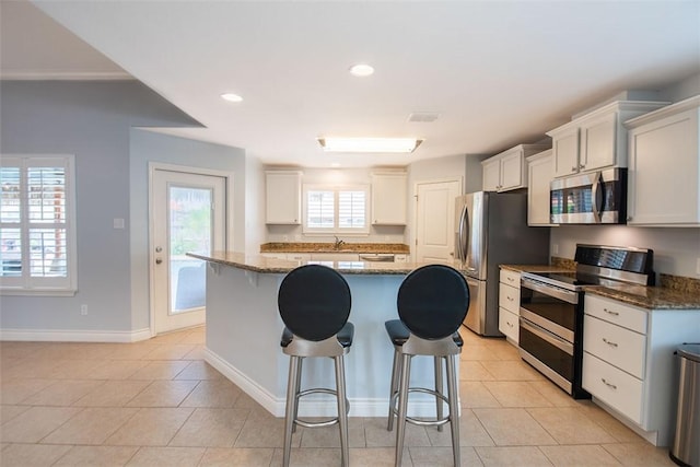 kitchen with a sink, stainless steel appliances, dark stone countertops, a kitchen breakfast bar, and a center island