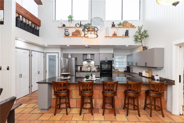 11157 Jackson Ter, Corpus Christi, TX 78410 - kitchen featuring gray cabinetry, wall chimney range hood, stainless steel refrigerator with ice dispenser, a towering ceiling, and a peninsula