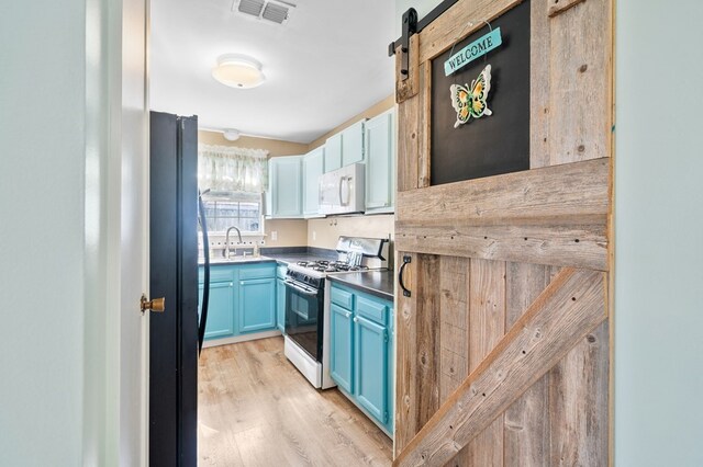 kitchen featuring visible vents, white microwave, a barn door, freestanding refrigerator, and gas range