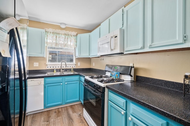 kitchen featuring white appliances, light wood finished floors, dark countertops, blue cabinetry, and a sink