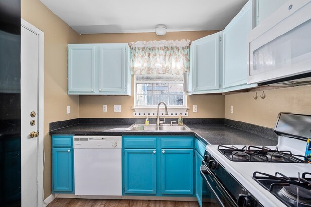 kitchen featuring dark countertops, white appliances, a sink, and blue cabinetry