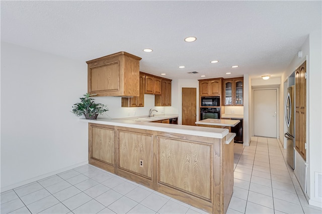 kitchen featuring kitchen peninsula, black appliances, a textured ceiling, light tile patterned floors, and sink