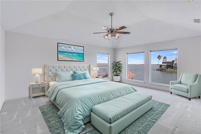 bedroom featuring a textured ceiling, a water view, ceiling fan, and light carpet