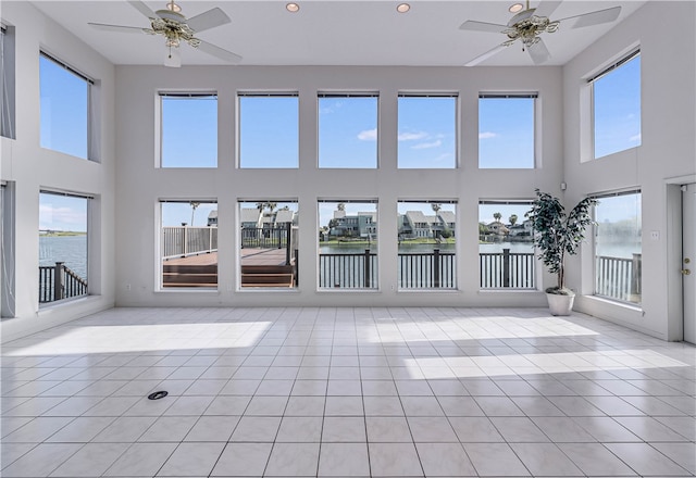 unfurnished sunroom featuring ceiling fan and a water view