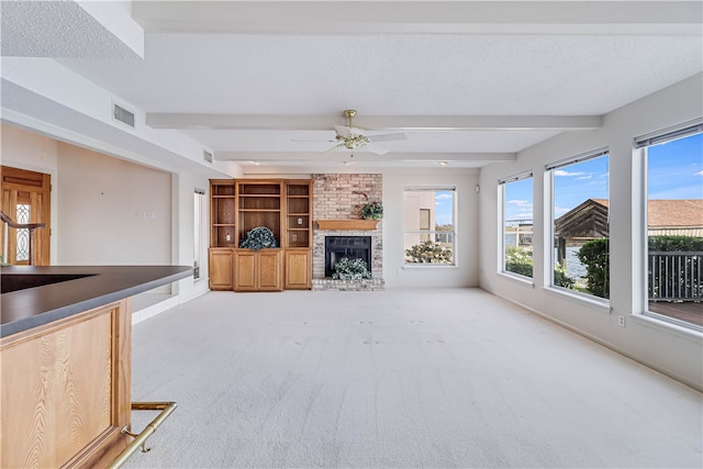 unfurnished living room with a textured ceiling, light colored carpet, ceiling fan, and beam ceiling