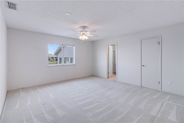 empty room featuring ceiling fan, light colored carpet, and a textured ceiling