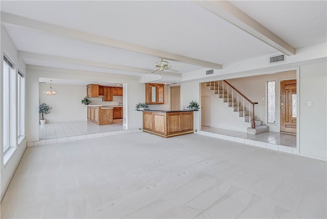 unfurnished living room with ceiling fan with notable chandelier, light colored carpet, and beamed ceiling