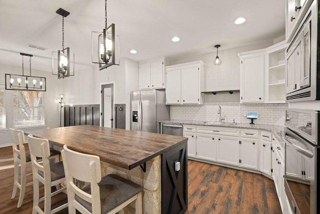 kitchen with appliances with stainless steel finishes, white cabinetry, sink, hanging light fixtures, and light stone counters