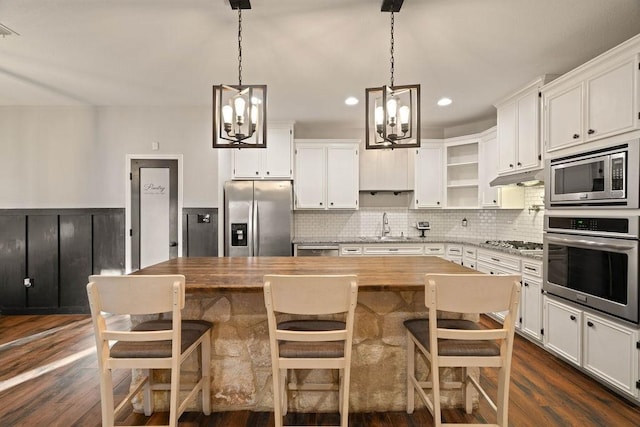 kitchen with butcher block counters, stainless steel appliances, a center island, white cabinets, and a kitchen bar