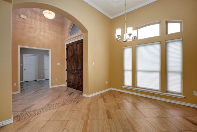 foyer featuring baseboards, arched walkways, an inviting chandelier, a high ceiling, and crown molding