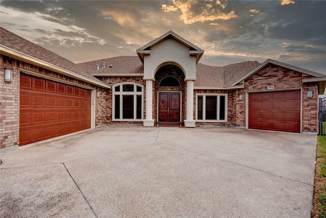 view of front of home with concrete driveway, brick siding, and roof with shingles