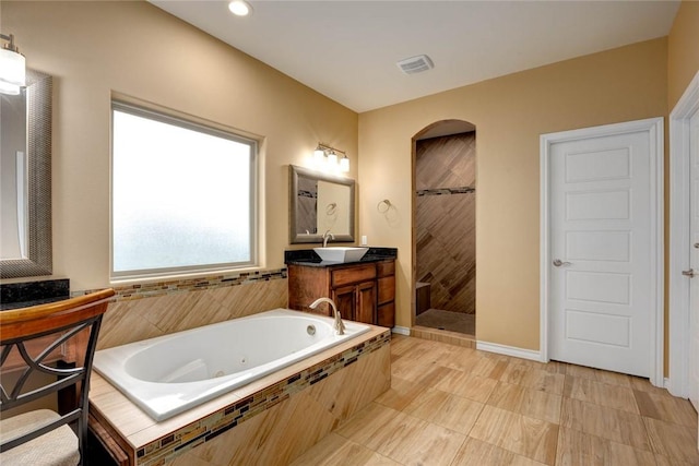 full bath featuring visible vents, baseboards, a tub with jets, a tile shower, and vanity