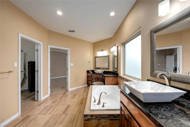 bathroom featuring baseboards, visible vents, a jetted tub, a sink, and two vanities