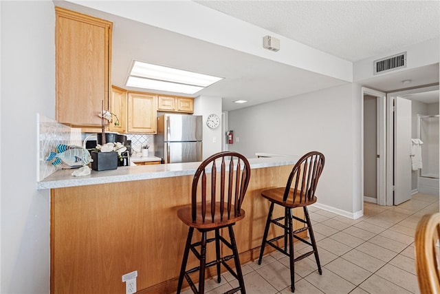 kitchen with kitchen peninsula, tasteful backsplash, a breakfast bar, stainless steel refrigerator, and light brown cabinetry